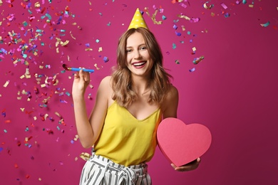 Photo of Young woman with birthday gift and party blower on color background