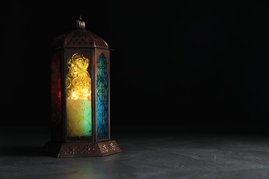 Photo of Decorative Arabic lantern on grey table against black background, space for text
