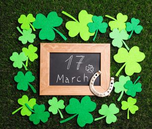 Photo of Flat lay composition with horseshoe and chalkboard on grass. St. Patrick's Day celebration