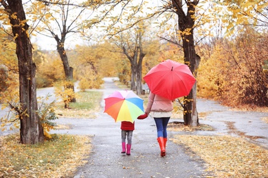 Mother and daughter with umbrellas taking walk in autumn park on rainy day