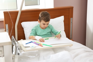 Photo of Little child with intravenous drip drawing in hospital bed