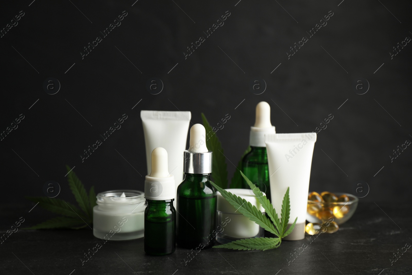 Photo of Composition with CBD oil, THC tincture and hemp leaves on black stone table