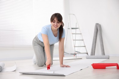 Photo of Woman applying glue onto wallpaper sheet in room