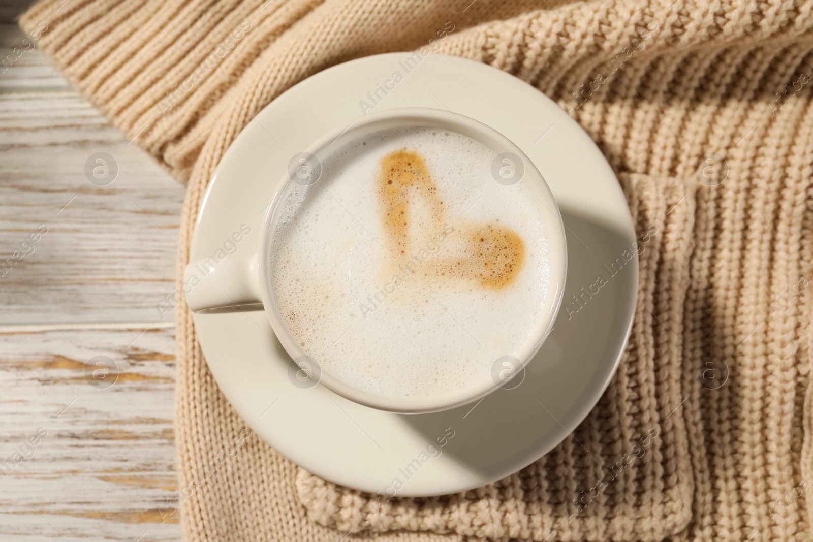 Photo of Cup of tasty coffee and sweater on white wooden table, top view