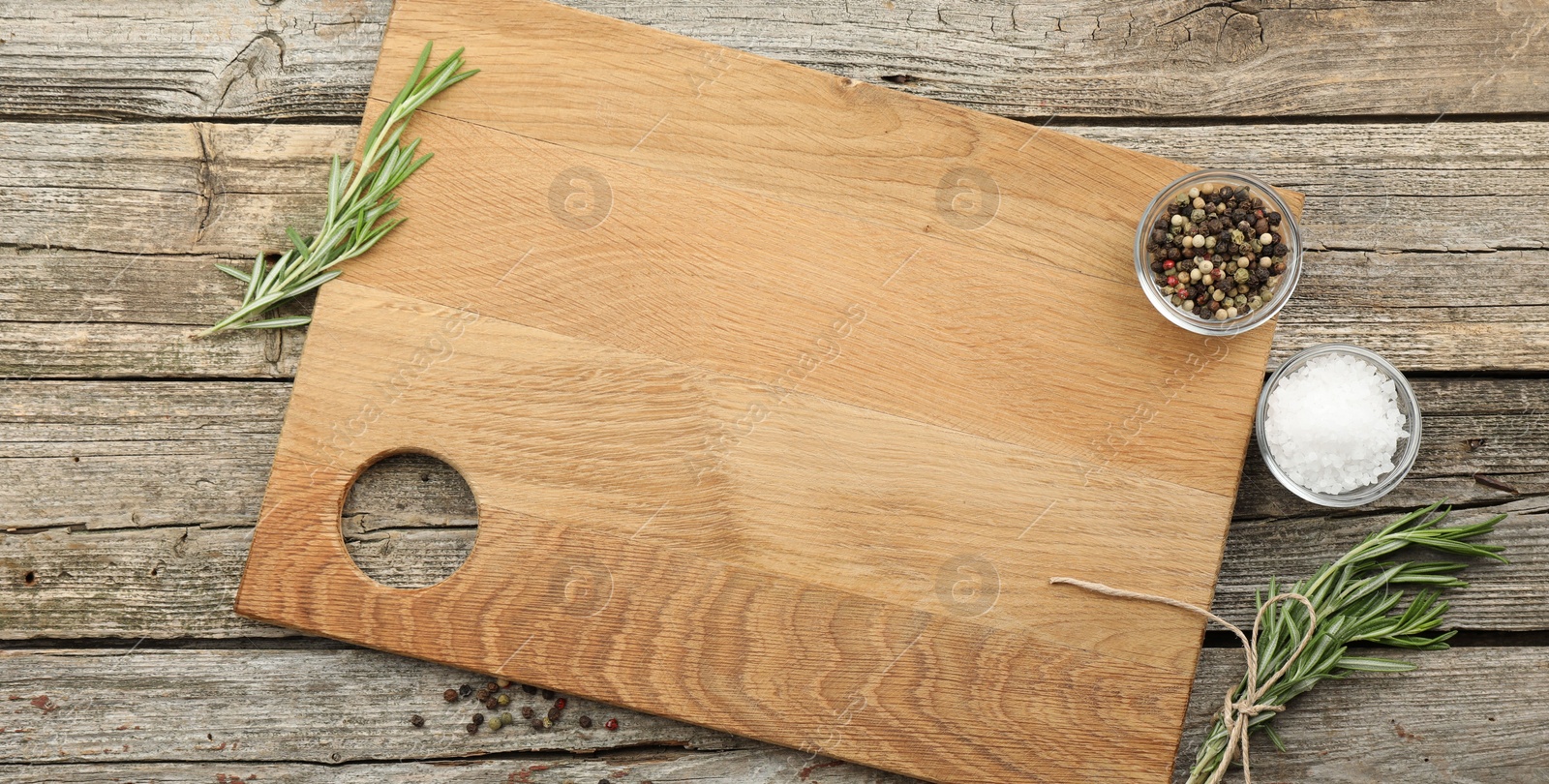 Photo of Cutting board, rosemary, salt and pepper on wooden table, flat lay. Space for text