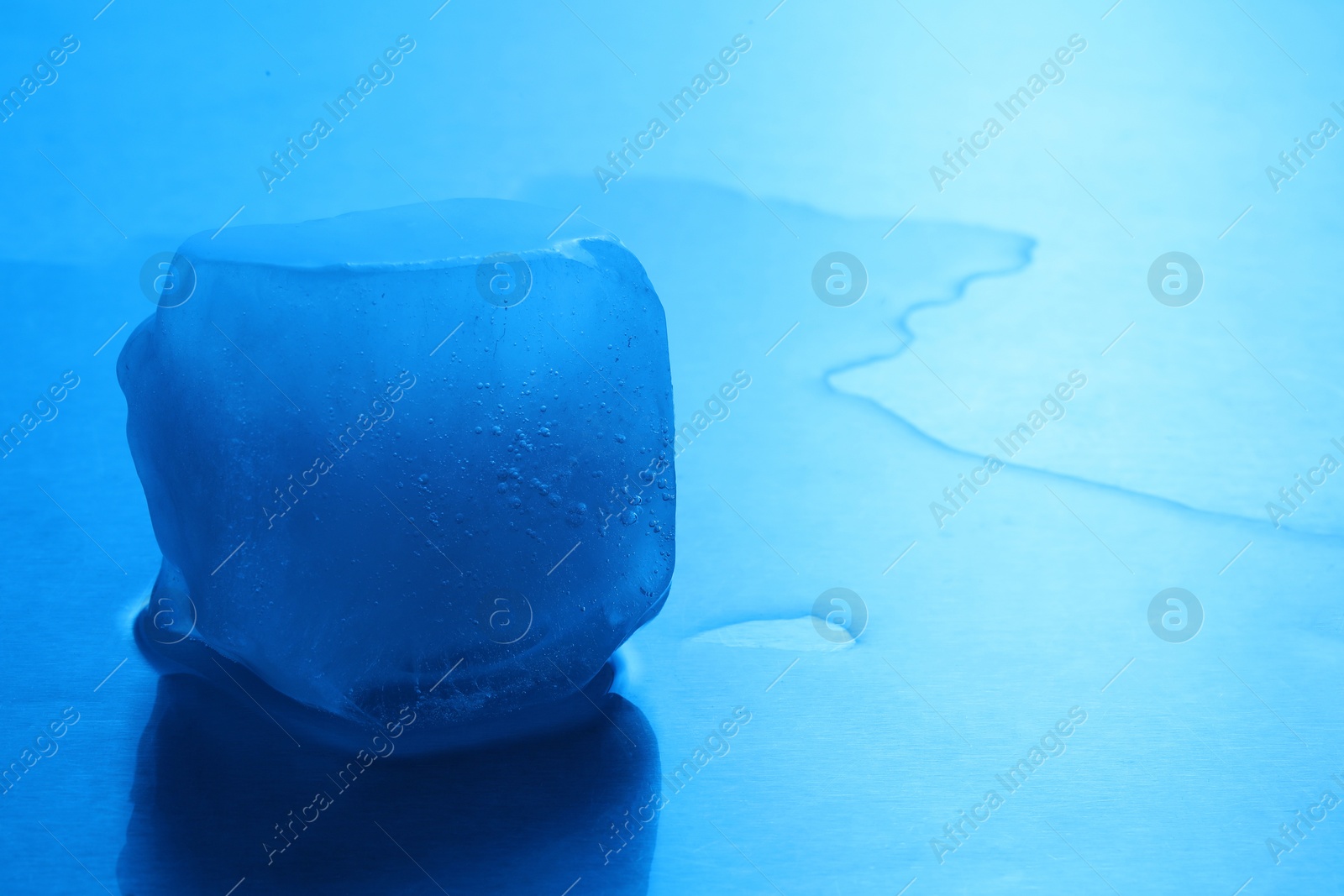 Photo of Crystal clear ice cube on light blue background, space for text. Color tone effect