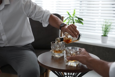 Photo of Young men drinking whiskey together at home, closeup