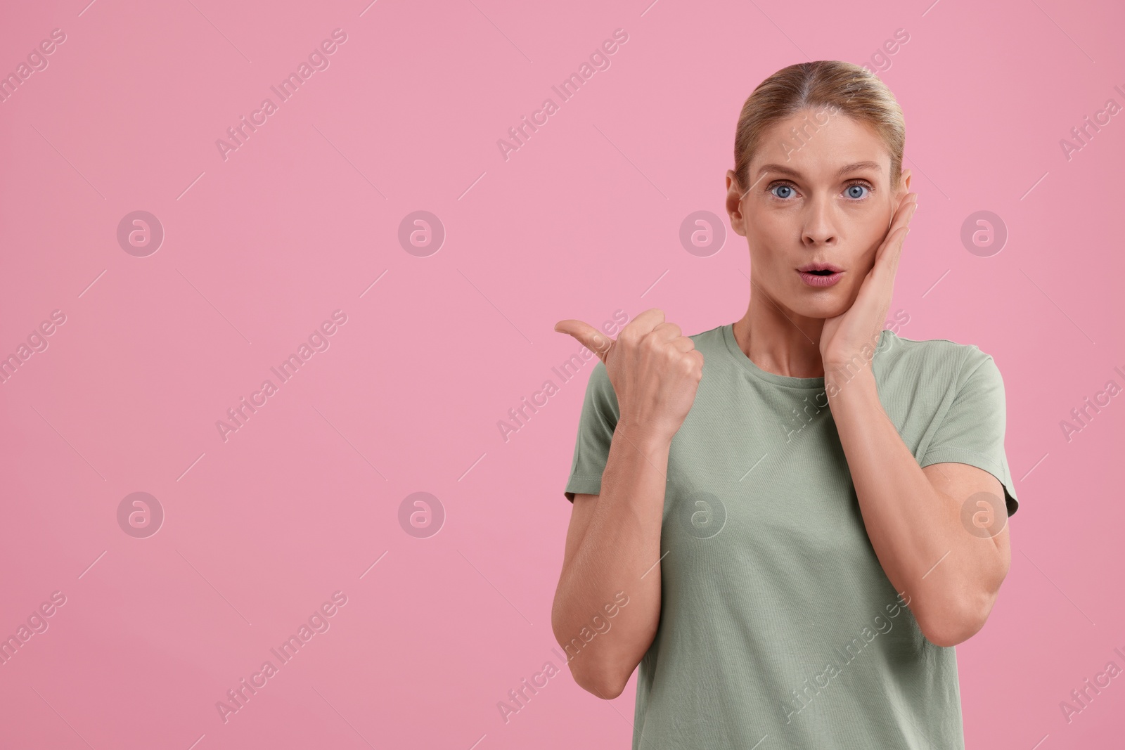 Photo of Special promotion. Surprised woman pointing at something on pink background. Space for text