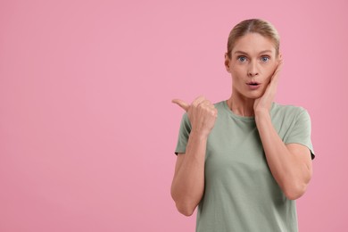 Photo of Special promotion. Surprised woman pointing at something on pink background. Space for text