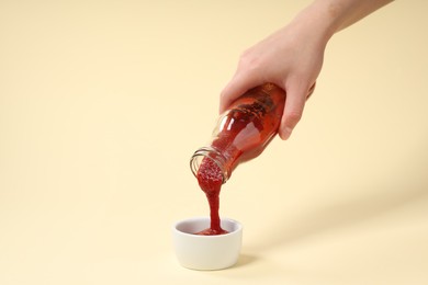 Woman pouring tasty ketchup from bottle into bowl on beige background, closeup. Space for text