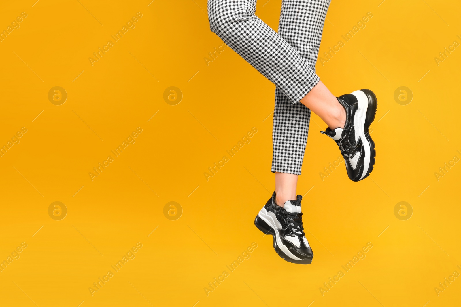 Photo of Woman wearing stylish sneakers on yellow background, closeup. Space for text