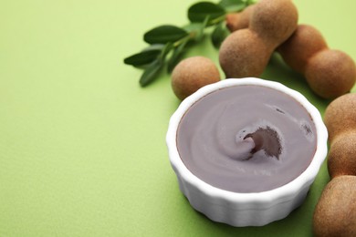Photo of Bowl of tasty tamarind sauce and fresh pods on light green table. Space for text