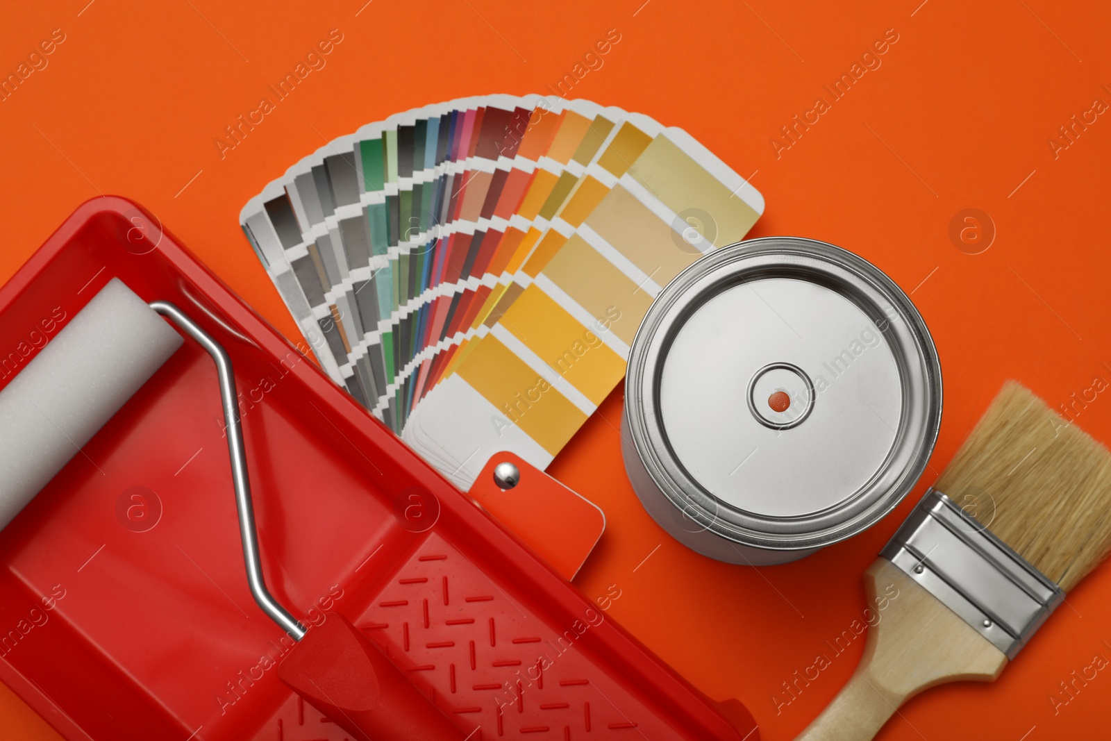 Photo of Can of paint, brush, roller, container and color palette samples on orange background, flat lay