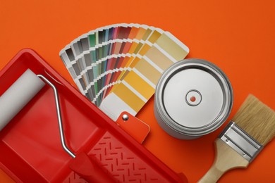 Photo of Can of paint, brush, roller, container and color palette samples on orange background, flat lay