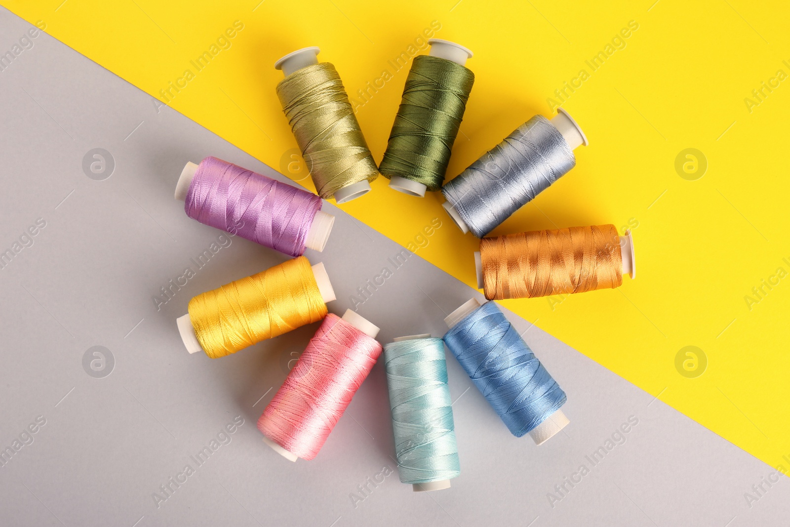 Photo of Different sewing threads on color background, flat lay