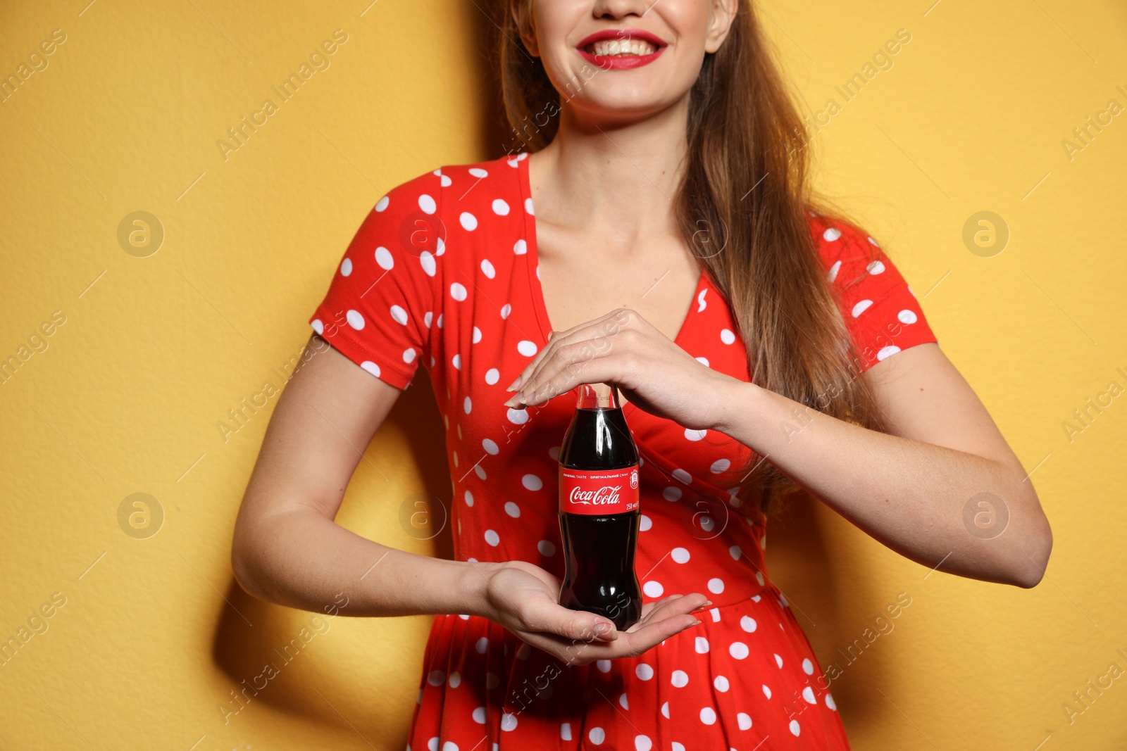 Photo of MYKOLAIV, UKRAINE - NOVEMBER 28, 2018: Young woman with bottle of Coca-Cola on color background