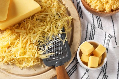 Photo of Grated, whole pieces of cheese and grater on cloth, top view