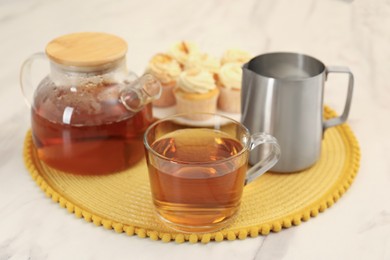 Photo of Aromatic tea in glass teapot, cup and pitcher on white marble table