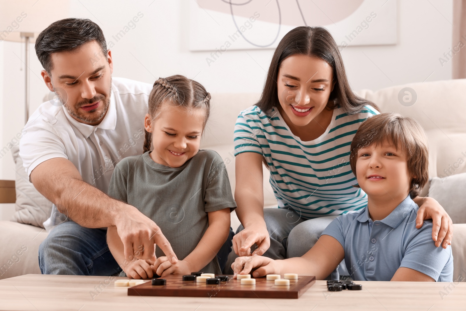 Photo of Parents playing checkers with children at table in room