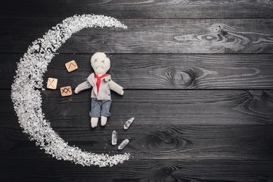 Voodoo doll pierced with pins and ceremonial items on black wooden table, flat lay. Space for text