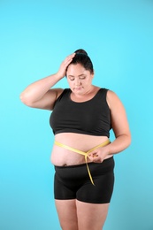 Fat woman with measuring tape on color background. Weight loss