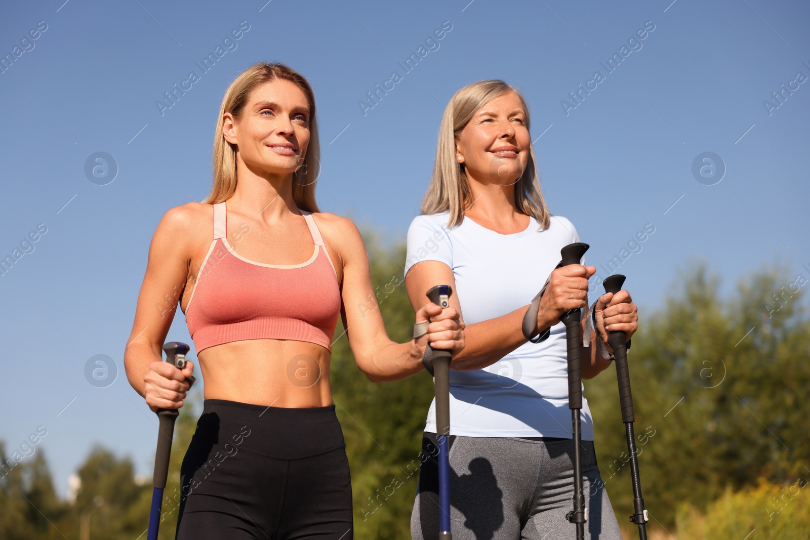 Photo of Happy women practicing Nordic walking with poles outdoors on sunny day