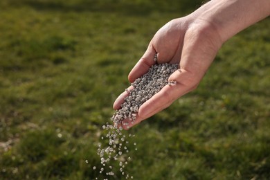 Photo of Man fertilizing green grass on sunny day, closeup