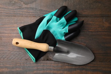 Pair of claw gardening gloves and trowel on wooden table, top view