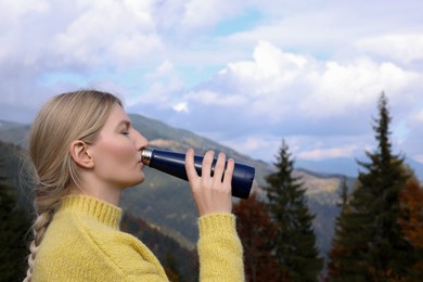 Photo of Young woman drinking hot beverage from thermo bottle in mountains