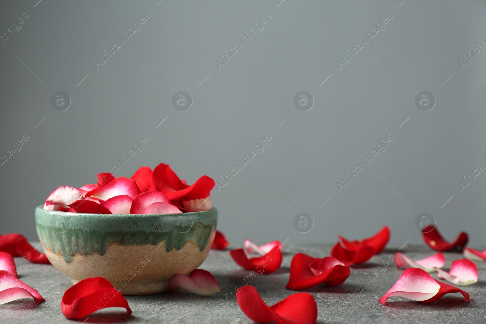 Photo of Bowl with rose petals on grey table, space for text