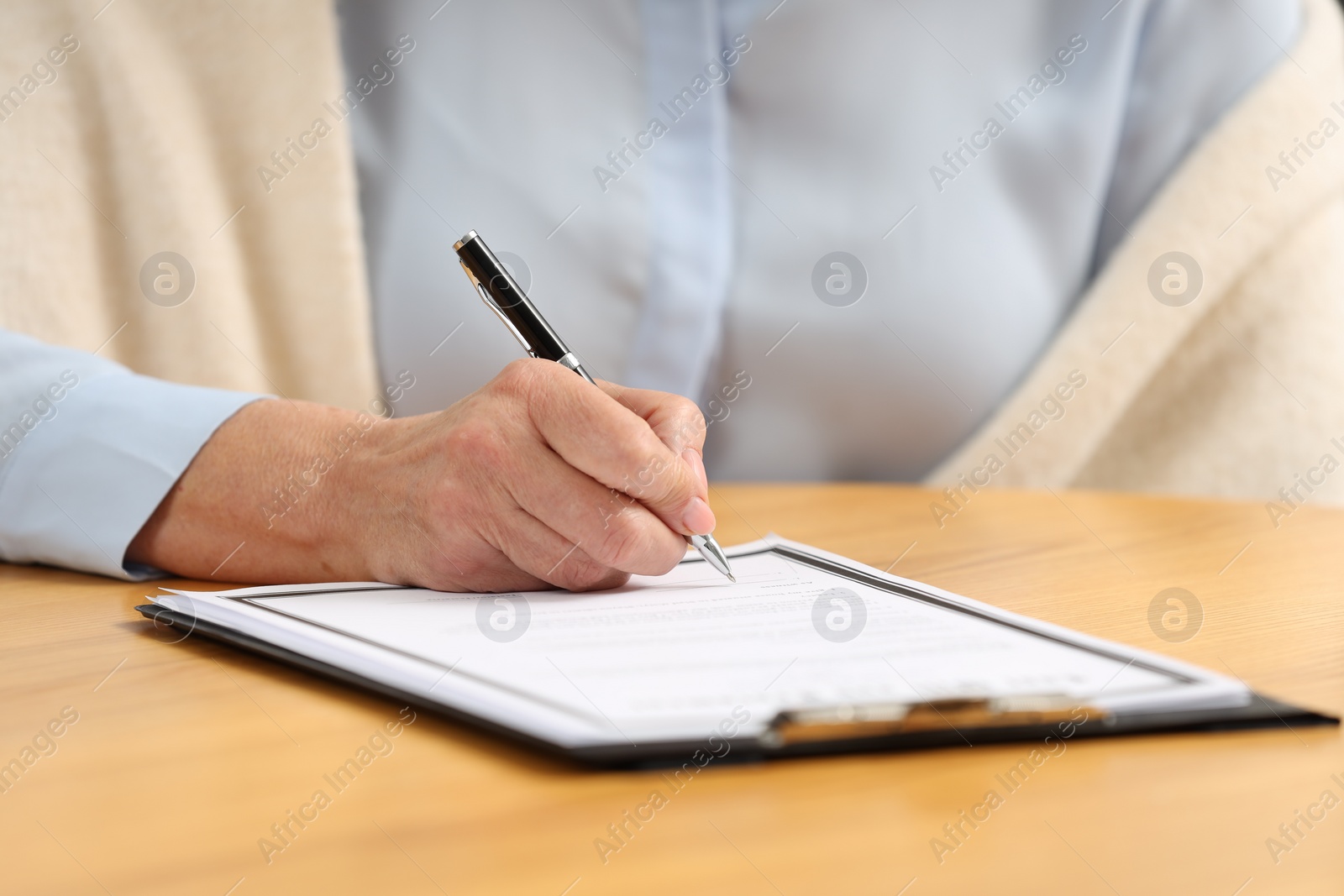 Photo of Senior woman signing Last Will and Testament at wooden table, closeup