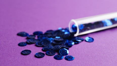 Photo of Tube with many blue sequins on purple background, closeup