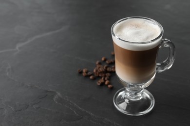 Photo of Glass cup of delicious layered coffee and beans on black table, space for text