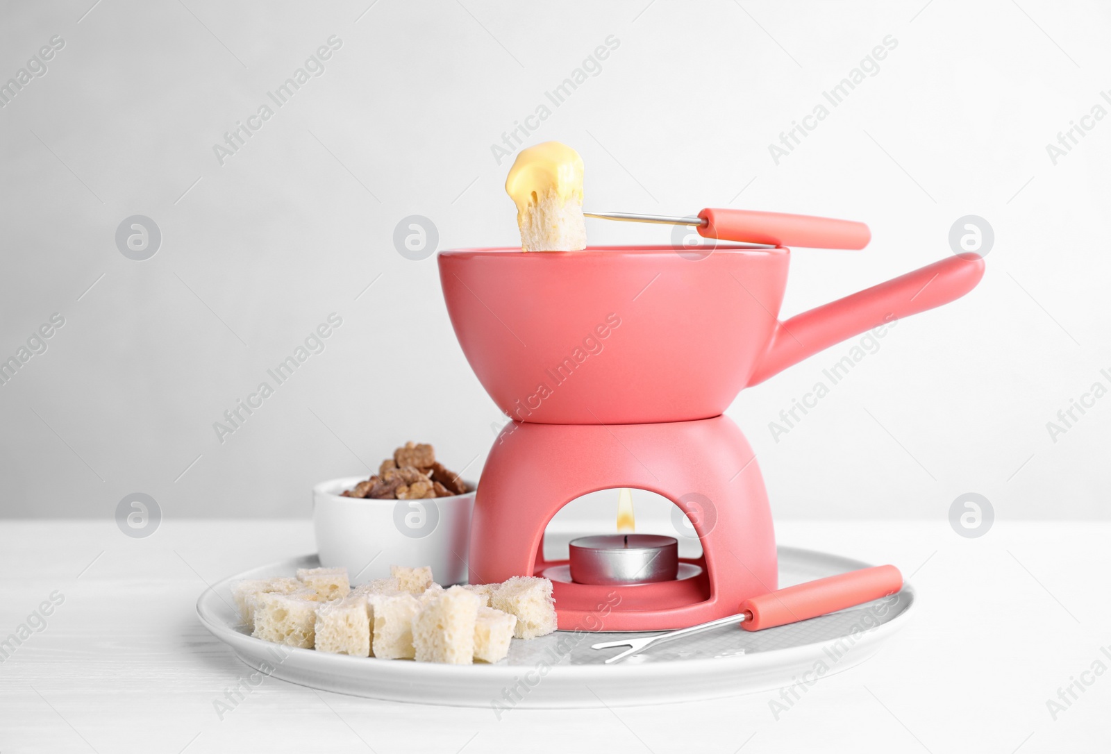 Photo of Plate with pot of cheese fondue, bread and walnuts on white table