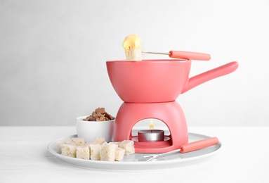 Plate with pot of cheese fondue, bread and walnuts on white table