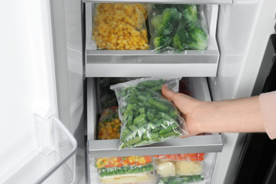 Woman taking plastic bag with frozen green beans from refrigerator, closeup