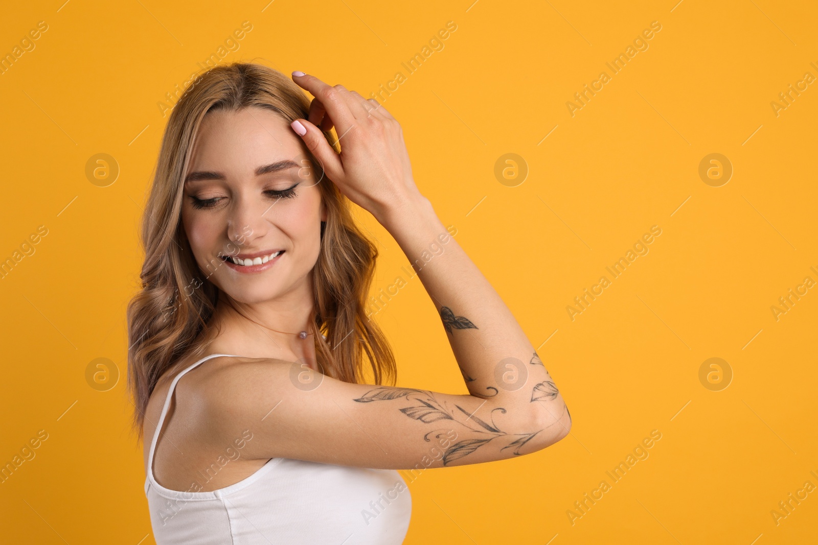 Photo of Beautiful woman with tattoos on arm against yellow background. Space for text