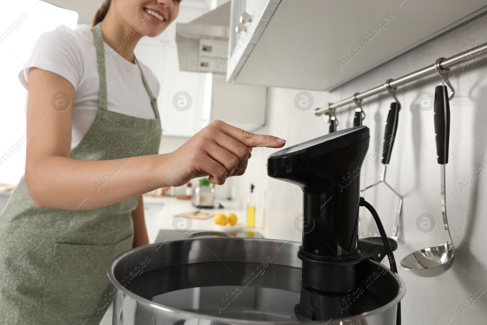 Photo of Woman using thermal immersion circulator in kitchen, closeup. Sous vide cooking