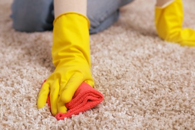 Woman in rubber gloves cleaning carpet with rag indoors, closeup. Space for text