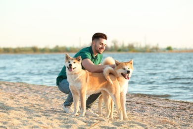 Photo of Young man walking his adorable Akita Inu dogs near river