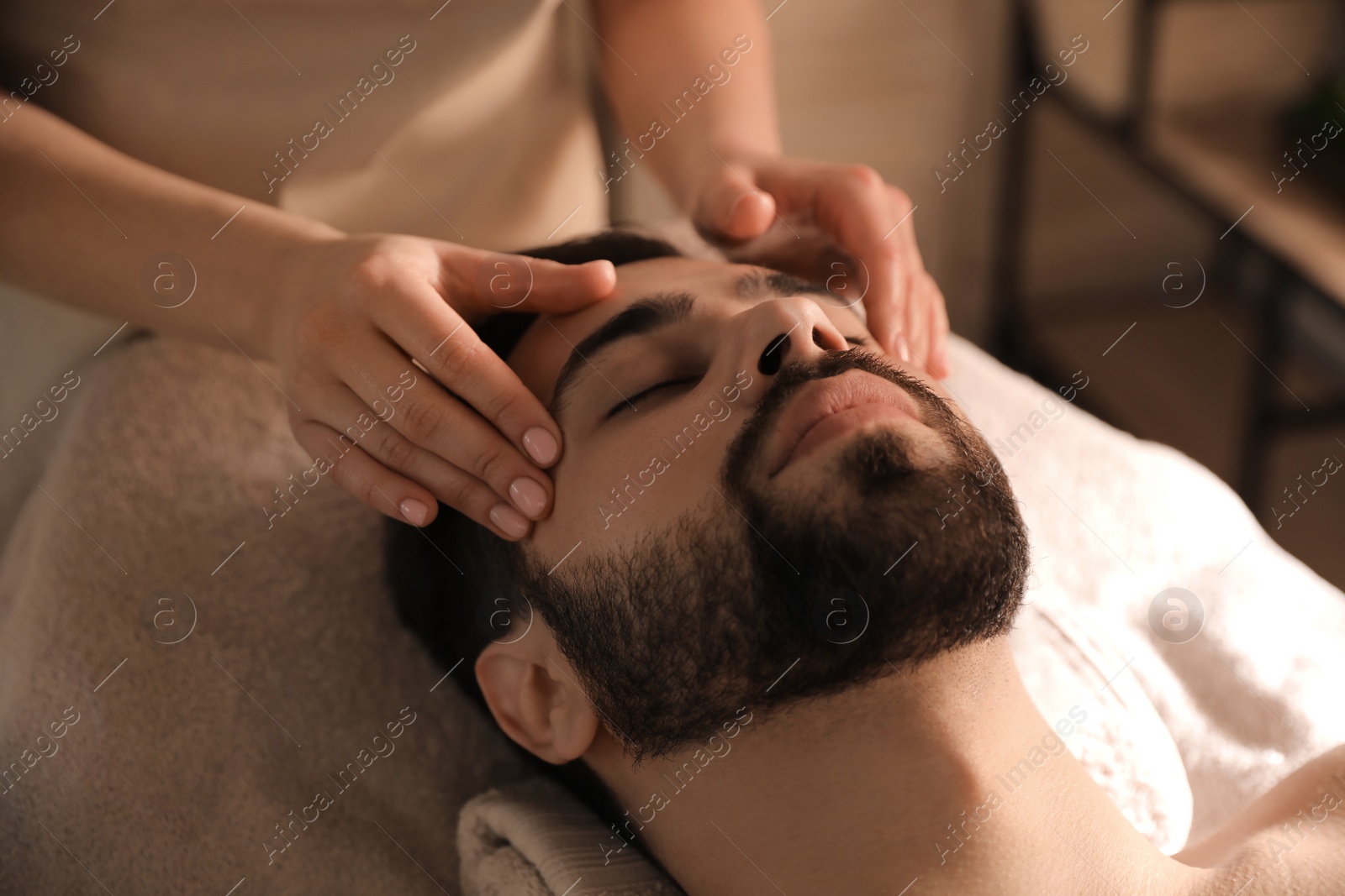 Photo of Young man receiving facial massage in beauty salon