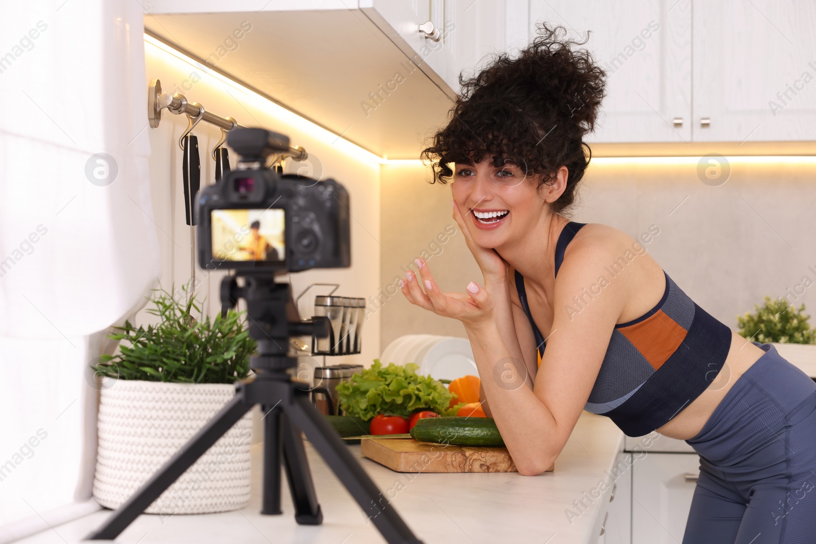 Photo of Smiling food blogger explaining something while recording video in kitchen