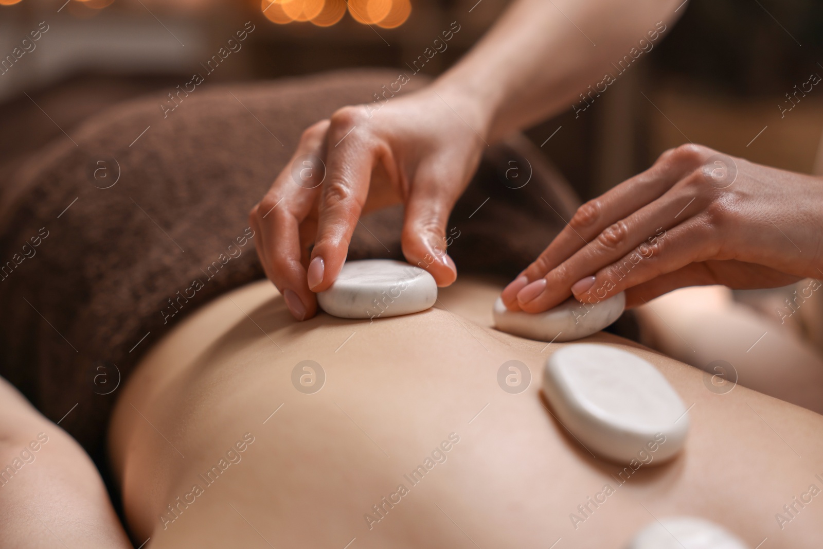 Photo of Spa therapy. Beautiful young woman lying on table during hot stone massage in salon, closeup