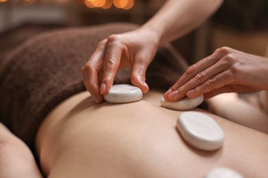 Photo of Spa therapy. Beautiful young woman lying on table during hot stone massage in salon, closeup