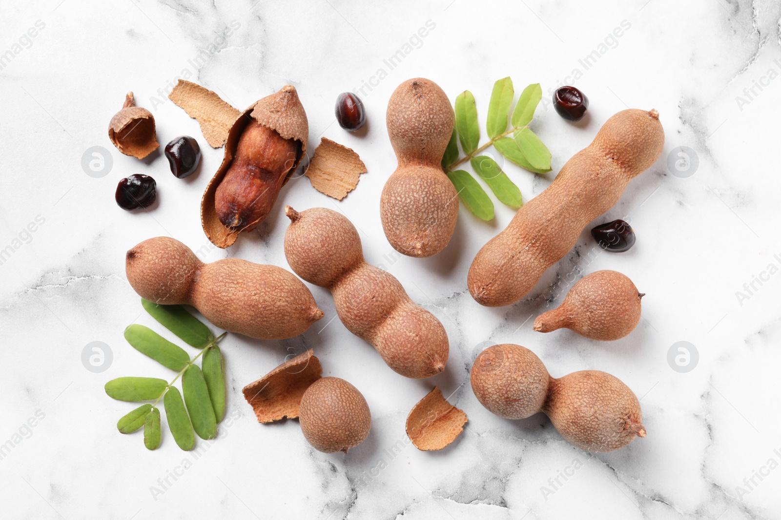 Photo of Ripe tamarinds and fresh leaves on white marble table, flat lay