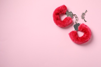 Photo of Red furry handcuffs and keys on pink background, top view with space for text. Sex toy