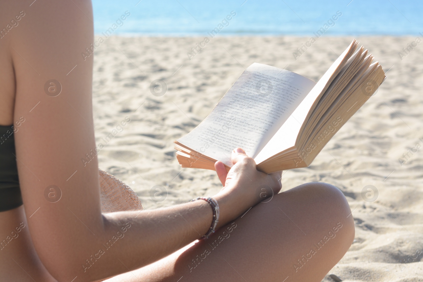 Photo of Woman reading book on sandy beach near sea, closeup