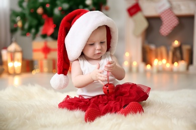 Photo of Cute baby in Santa hat playing with jingle bell at home. Christmas celebration