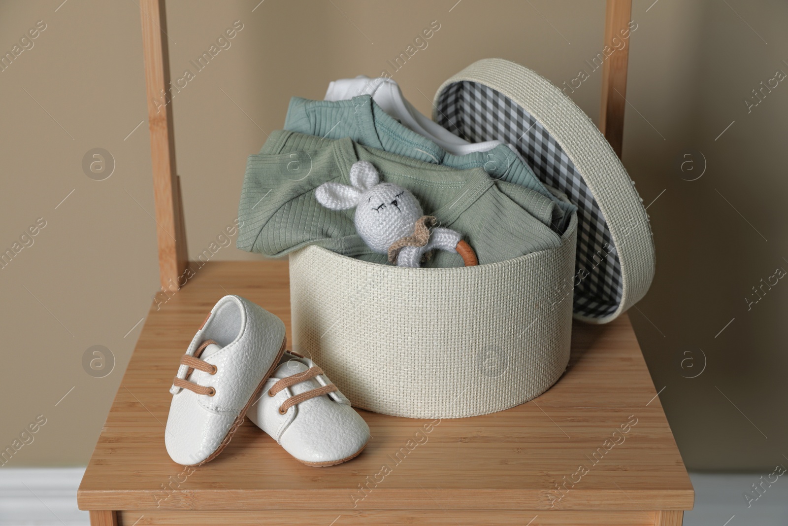 Photo of Box with baby bodysuits, booties and toy on chair indoors