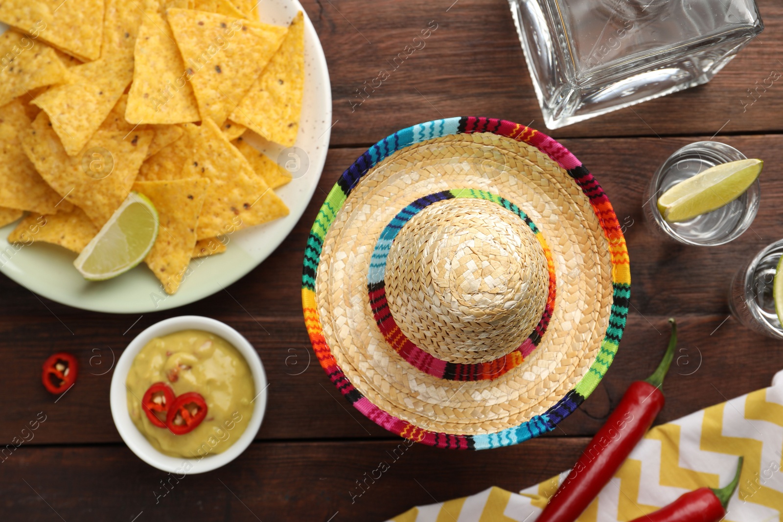Photo of Mexican sombrero hat, tequila with lime, chili peppers, nachos chips and dip sauce on wooden table, flat lay